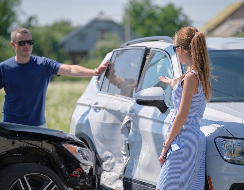 Male and female drivers talking about partial fault in a car accident; drivers partly at fault