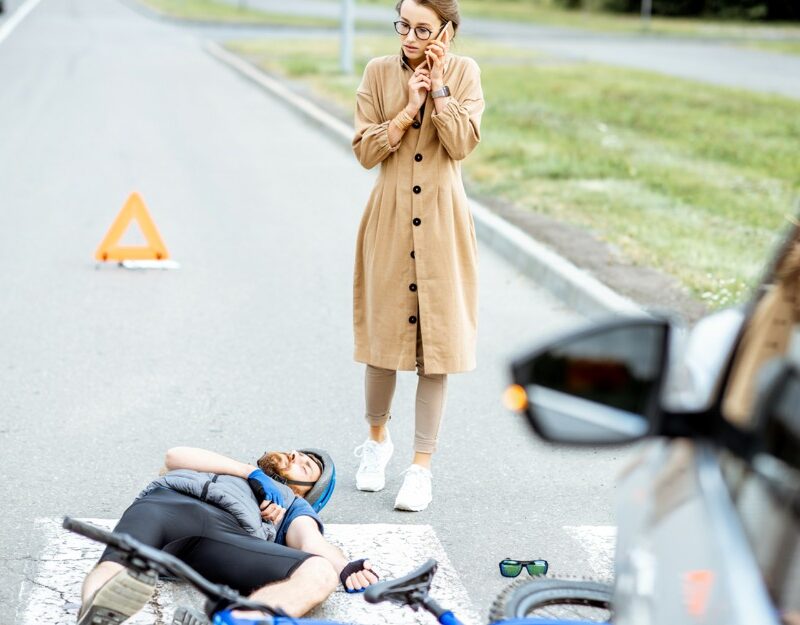 man on the road after bicycle accidents, woman is calling emergency services