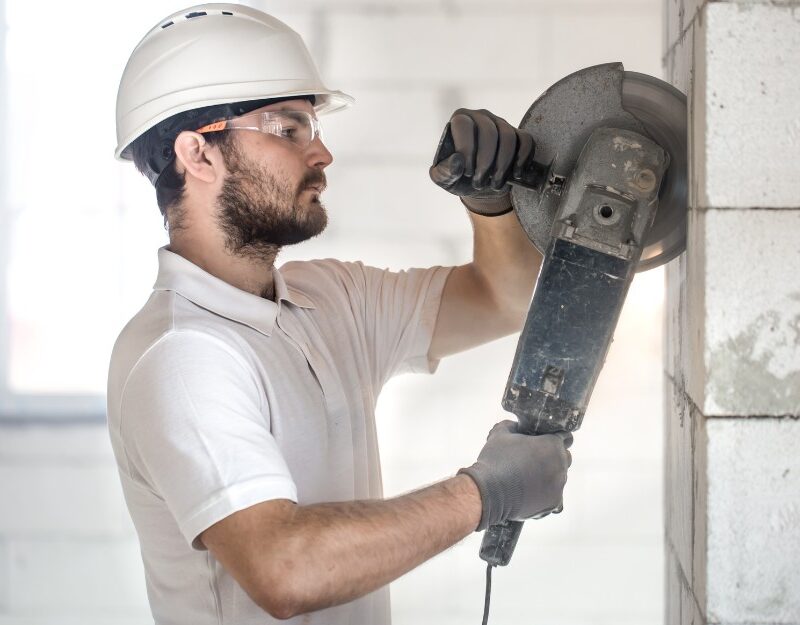 Male construction worker, without earmuffs, using a grinder to cut bricks on wall, may be eligible for compensation for hearing loss at work