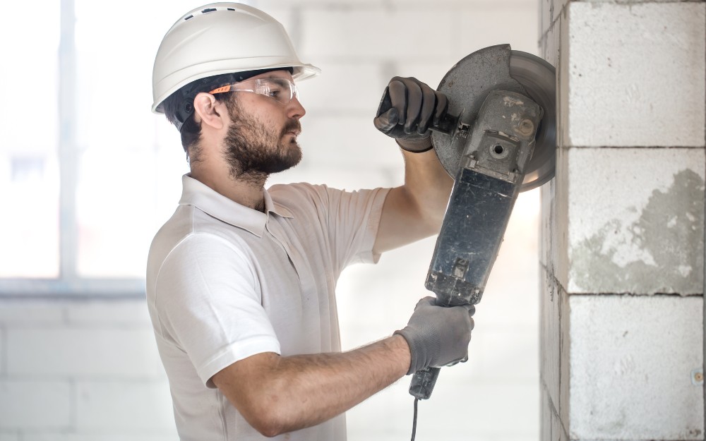 Male construction worker, without earmuffs, using a grinder to cut bricks on wall, may be eligible for compensation for hearing loss at work