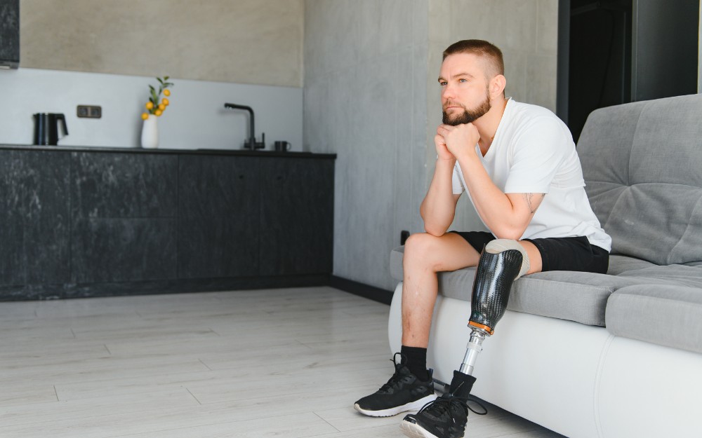 Man with a prosthesis, sitting on a sofa, contemplating about a loss of limb compensation claim